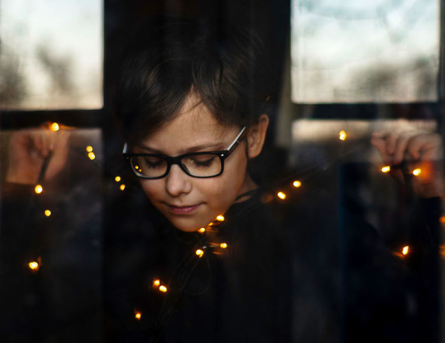 Portrait of boy holding garland lights seen through window