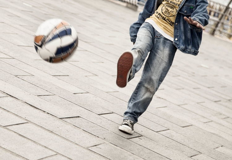 Low section of young man playing soccer on paved street