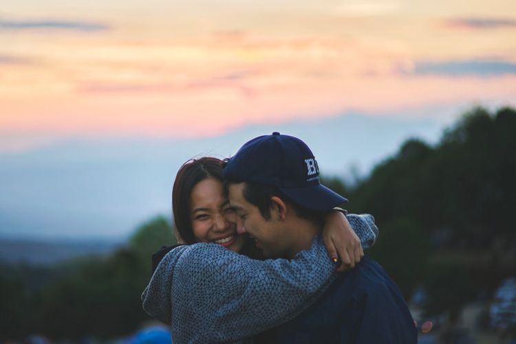 Young couple kissing against sky during sunset