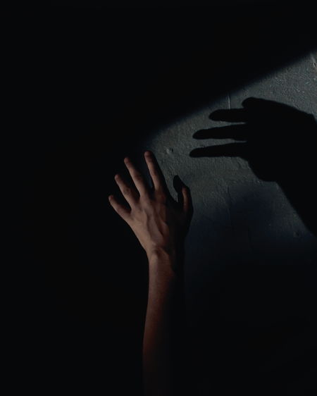 Close-up of hand touching shadow on wall in darkroom