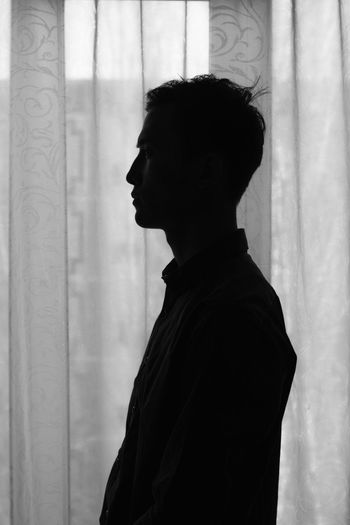 Side view of silhouette man standing against curtain at home