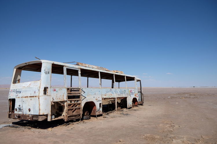 Old damaged bus on field against clear blue sky