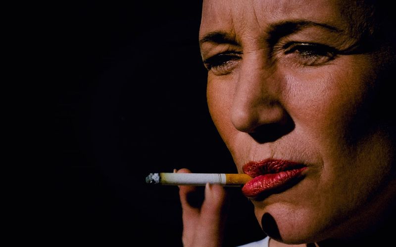 Close-up portrait of woman smoking cigarette against black background