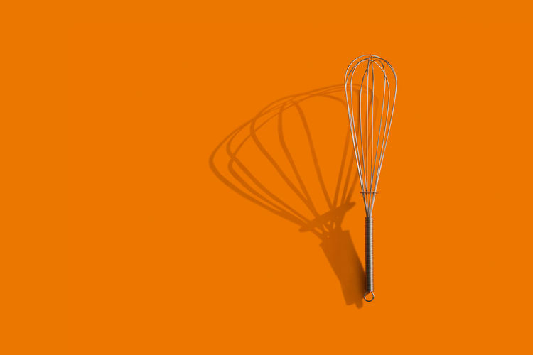 Directly above view of wire whisk over orange background