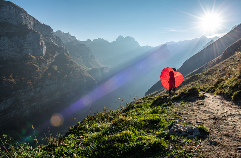Woman with red heart shape umbrella on mountain during sunny day