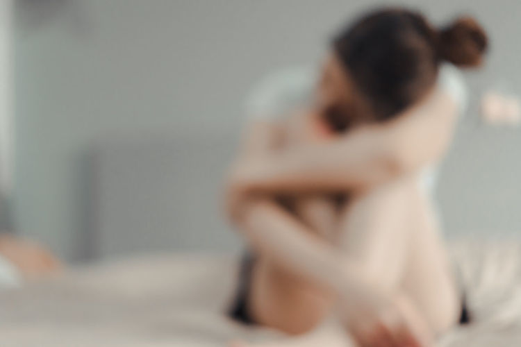 Midsection of woman sitting on bed at home