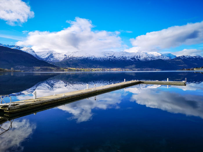 Scenic view of a boat dock in norwegian fjord and mountains against blue sky