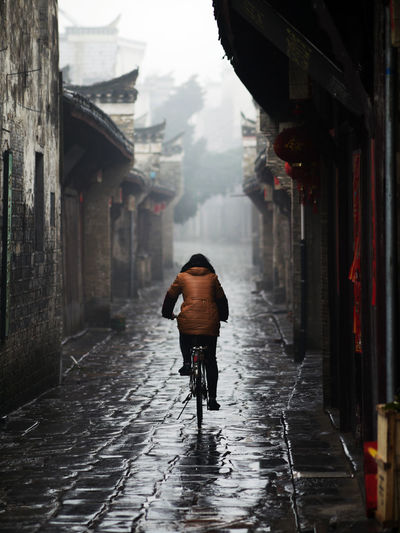 Rear view of person cycling on wet road during rainy season