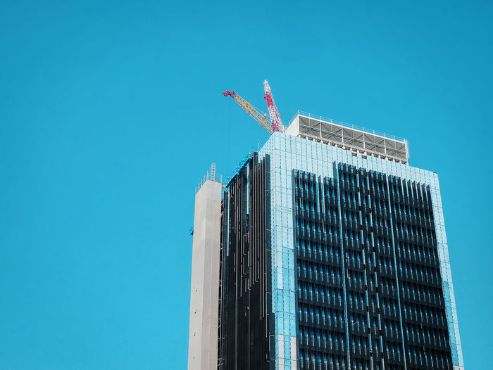 Low angle view of under construction building with cranes on the roof floor