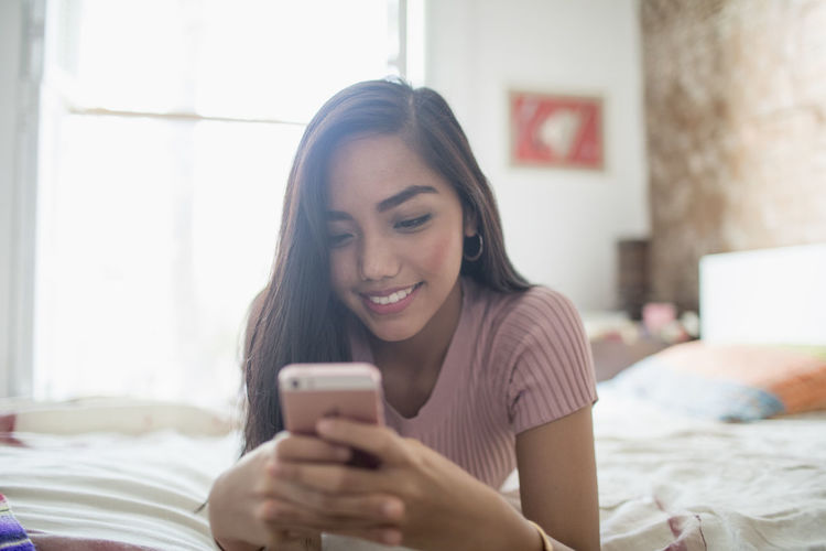 Young woman using her smartphone on her bed