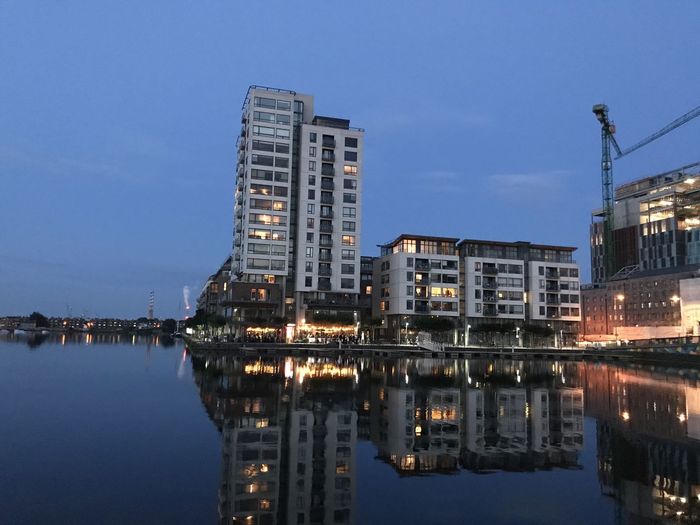 Illuminated buildings by lake against sky at night