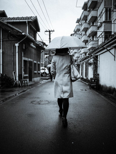 Rear view of woman holding umbrella while walking on street amidst buildings