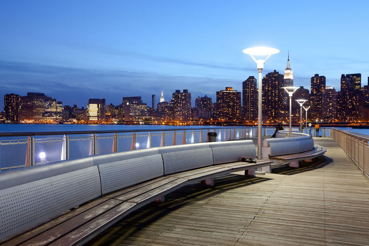 Pier over river against illuminated buildings in city