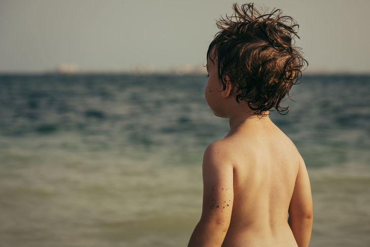 A little boy stands on the shore and looks at the sea.