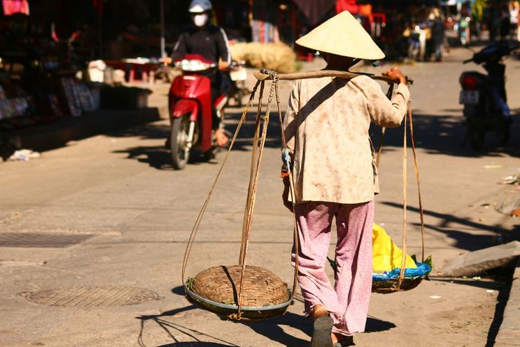 Rear view of a vietnamese woman walking carrying baskets called a shoulder pole