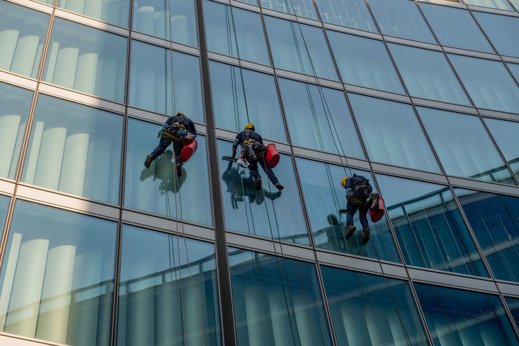Milan italy march 29 2021 skilled glass cleaners who lower themselves with slings from above