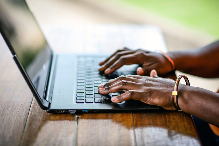 Cropped hands of man using laptop on wooden table