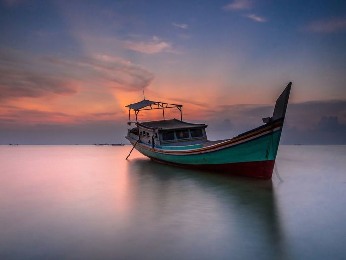 Boat moored in sea against sky during sunset