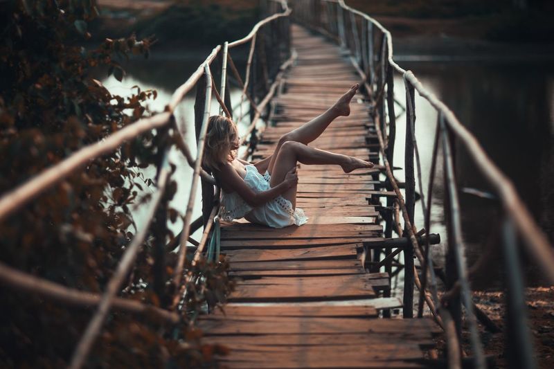 Side view of woman sitting on wooden footbridge
