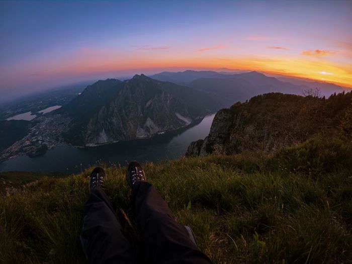 Low section of man sitting on mountain against sky during sunset