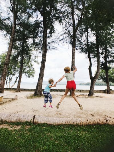 Full length rear view of woman and daughter jumping on sand