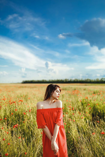 Young woman standing on field against sky