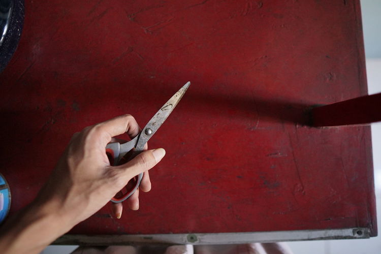 Cropped hand of man holding scissors on table