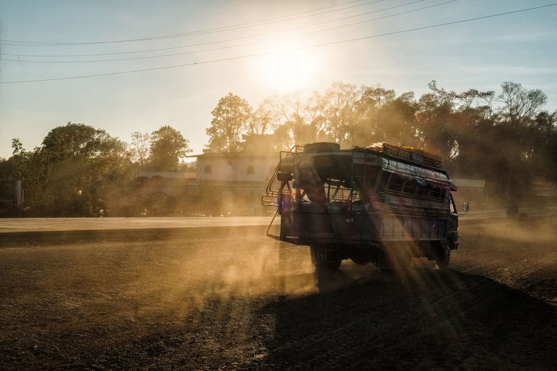 Vehicle moving on dirt road against sky during sunset