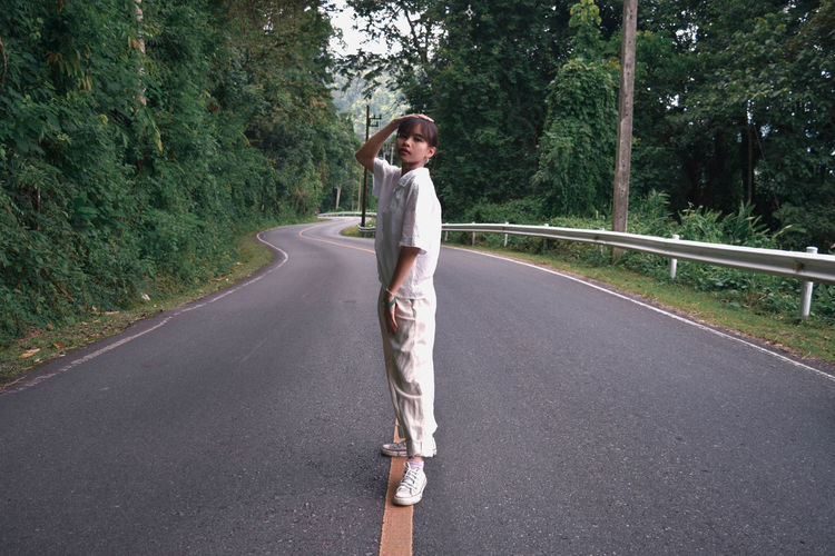 Portrait of young woman standing on road amidst trees