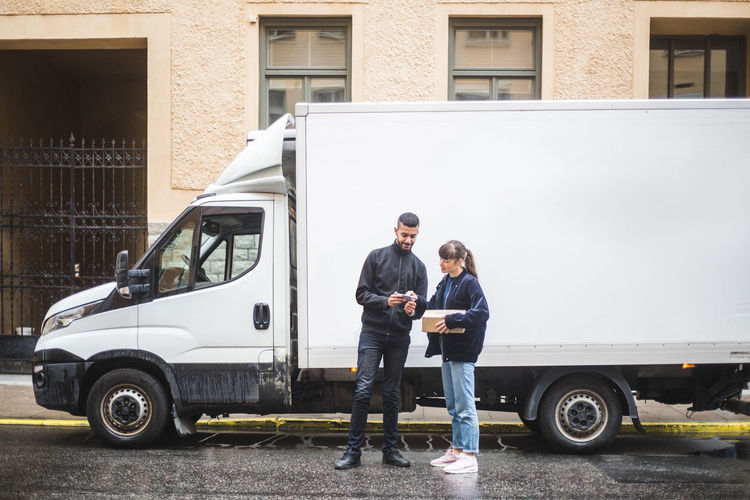 Young woman signing on mobile phone while receiving package from male mover