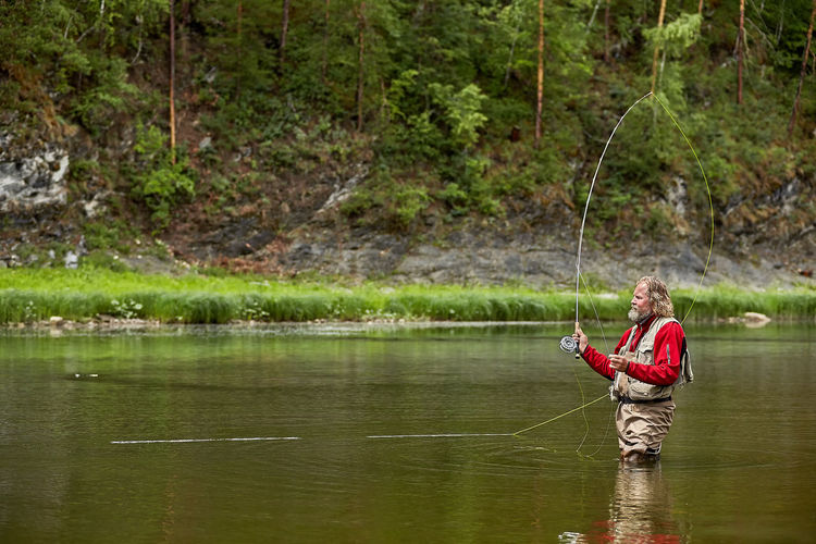 Man fishing in lake against trees