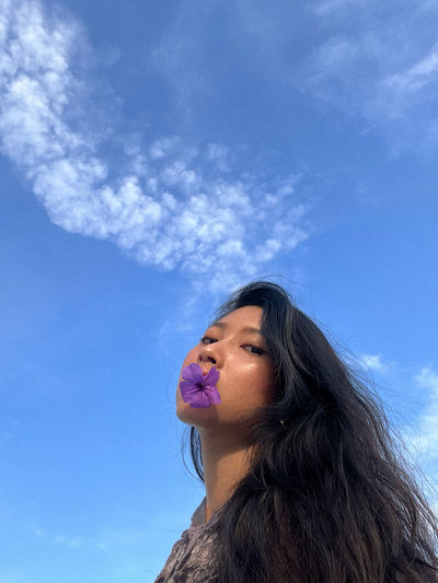 Low angle view of young woman drinking water against blue sky