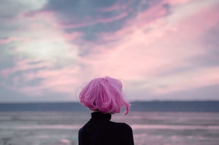 Woman with pink hair standing at beach against sky during sunset