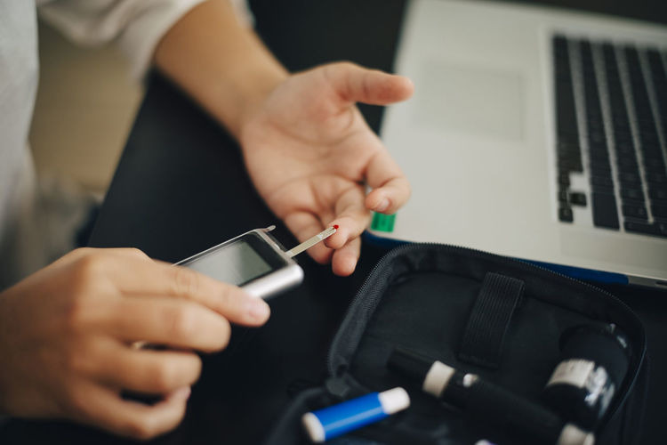 Cropped hands of businesswoman checking blood sugar level with glaucometer at desk