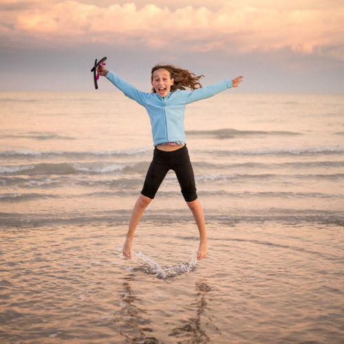 Full length portrait of smiling young woman jumping on beach