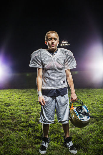 Portrait of football player holding helmet while standing on field