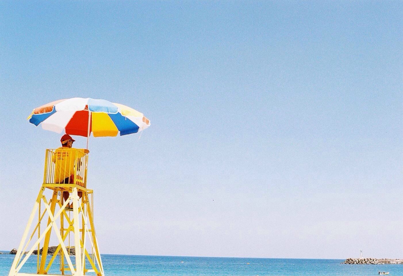 sea, clear sky, horizon over water, water, copy space, blue, beach, tranquility, tranquil scene, scenics, flag, nautical vessel, nature, transportation, beach umbrella, beauty in nature, sky, protection, vacations, day