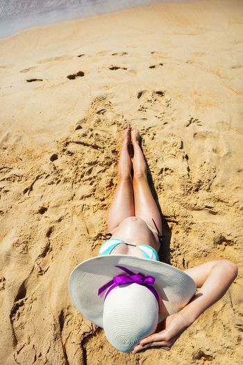 Low section of woman sitting at sandy beach