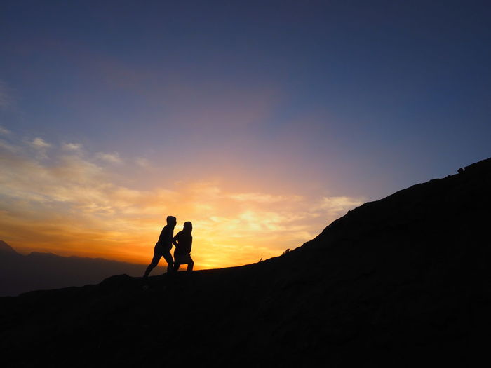 Silhouette men standing on mountain against sky during sunset