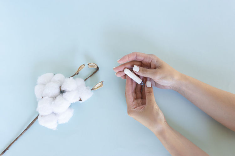 Woman hand holds a sanitary tampon with the cotton lying next to it