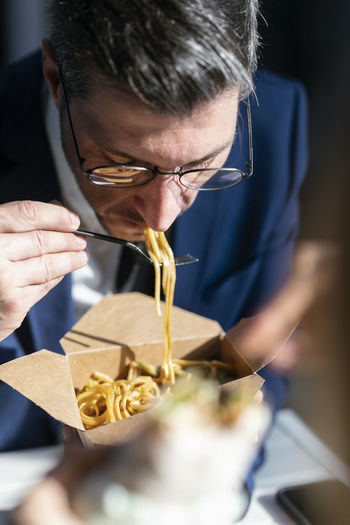 Businessman eating noodles while sitting in cafeteria at office