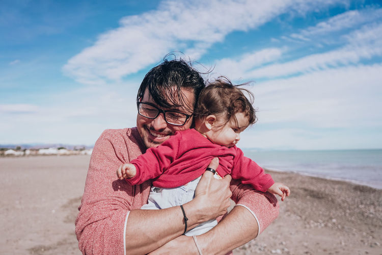 Father embracing daughter on beach against sky