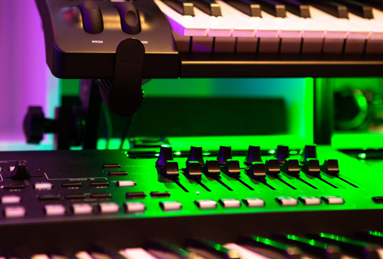 Closeup of electronic keyboard instrument and mixer nubs under green light.