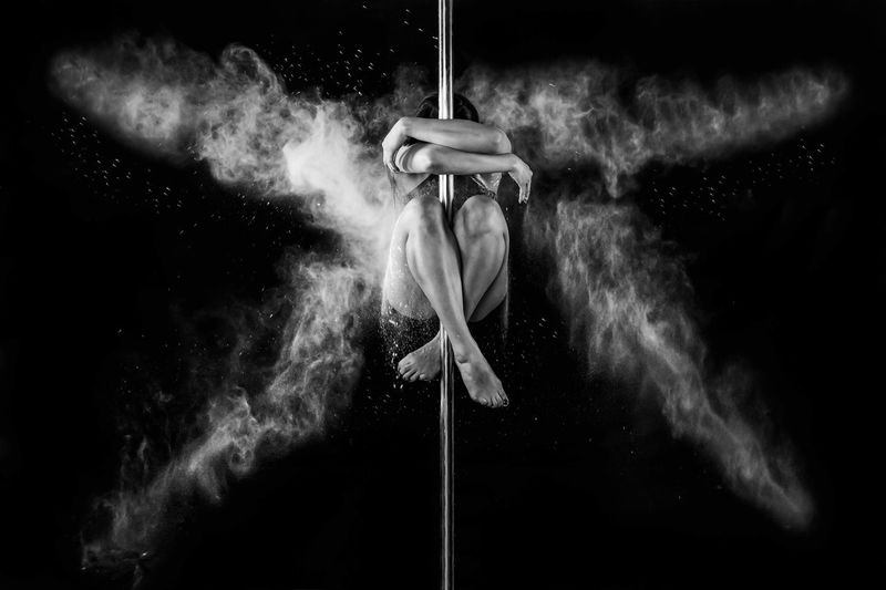 Woman embracing pole against black background
