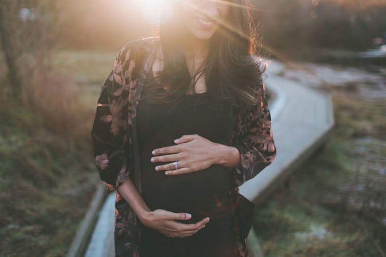 Midsection of pregnant woman standing at park during sunset