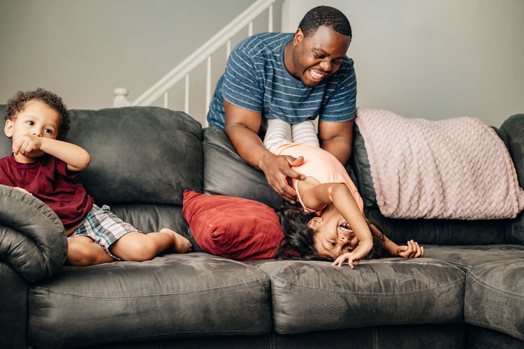 Father and kids at home playing on couch, african american or black father with his children