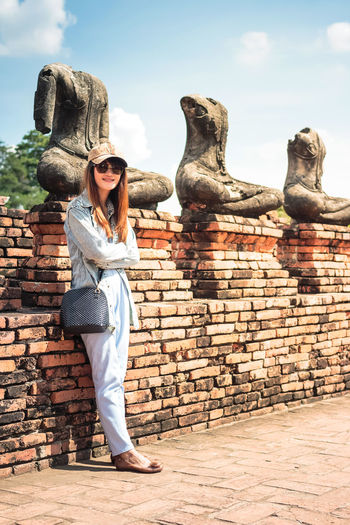 Full length of woman standing against statues on brick wall