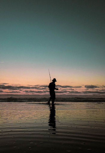 Silhouette man fishing in sea against sky during sunset