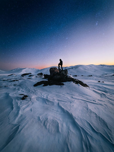 Man sitting on snow covered land against sky