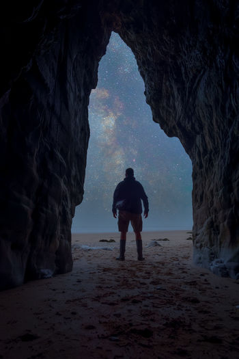 Rear view of man standing in sea cave looking at milky way